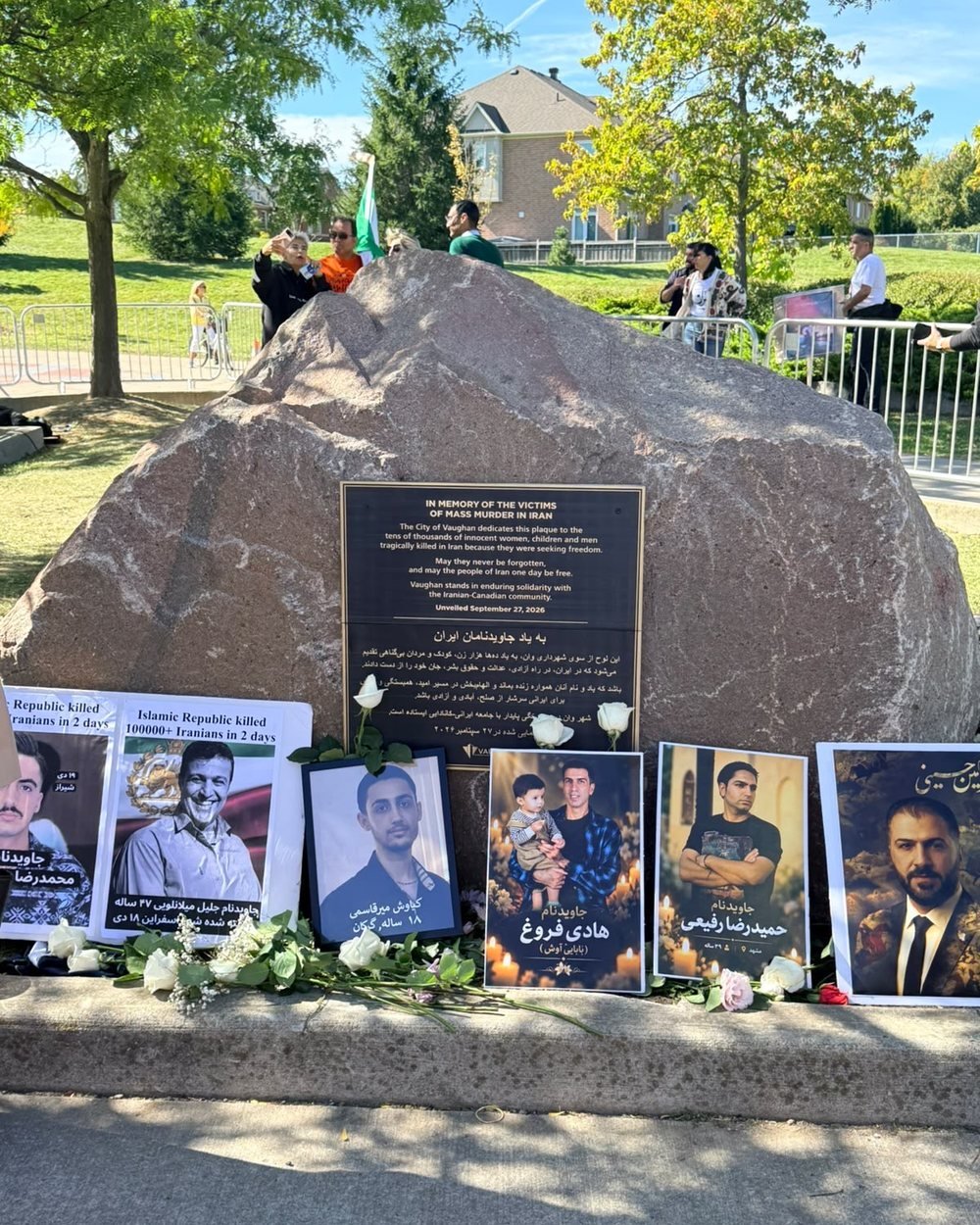 The permanent plaque commemorating the victims of mass killings in Iran, with portraits and white roses placed at its base